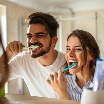 Couple smiling while brushing teeth in bathroom