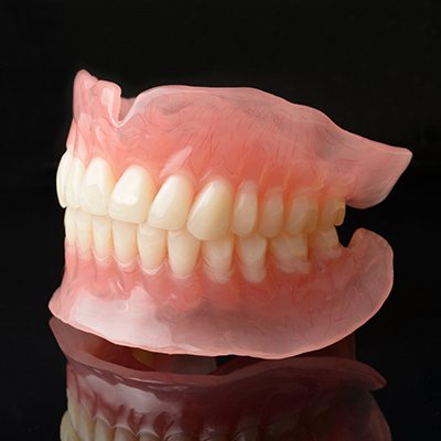 Close-up of full dentures on black reflective surface