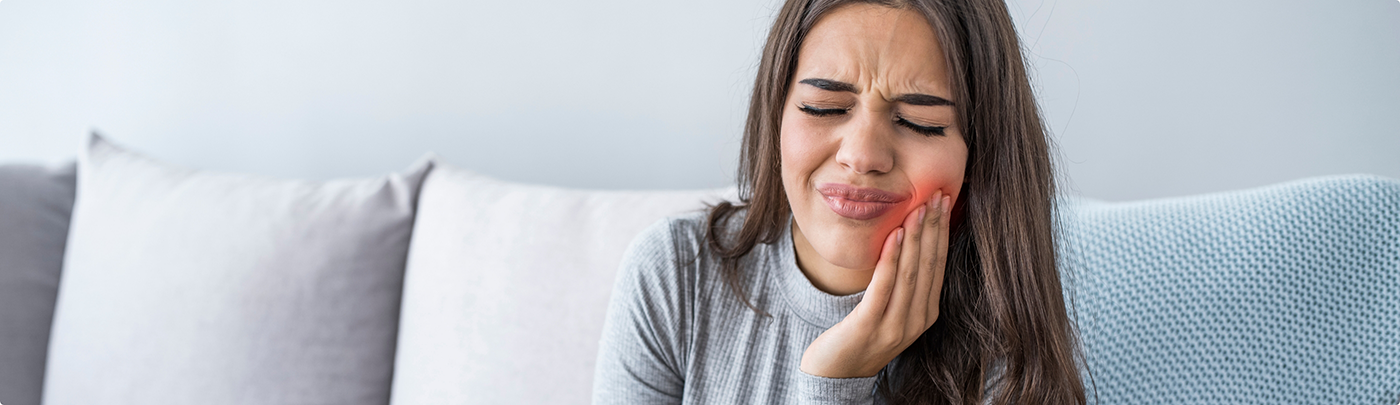 Woman holding her cheek in pain before seeing an emergency dentist in Little Elm