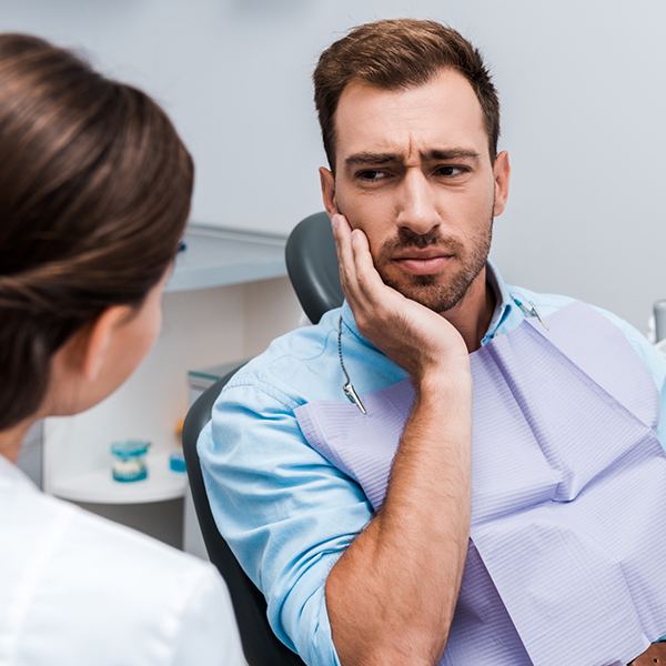 Man holding his cheek in pain while talking to his emergency dentist
