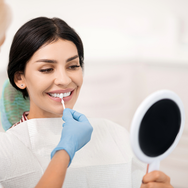Cosmetic dentist holding a veneer over a smiling patient's tooth