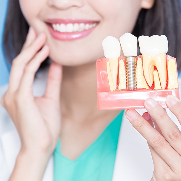 Dentist in white coat holding sample implant and touching hand to her jaw