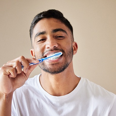 Man in white t-shirt brushing his teeth with standard toothbrush