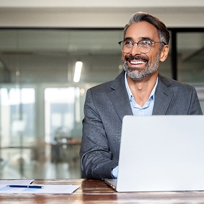 Man with silver hair in grey suit working on a laptop
