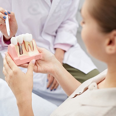 Dentist pointing to sample implant held by patient