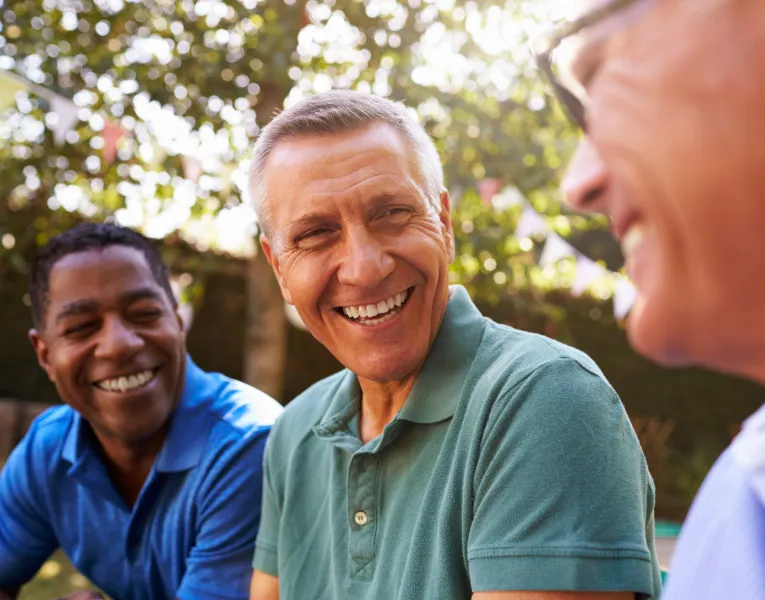 Three men laughing together outdoors on a sunny day